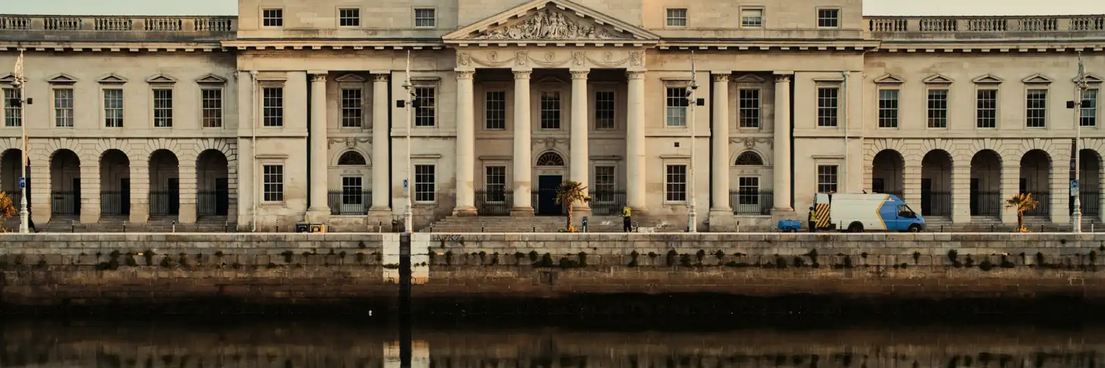 A fachada neoclássica da Custom House, em Dublin, com a colunata e o frontão refletidos nas águas do rio Liffey.