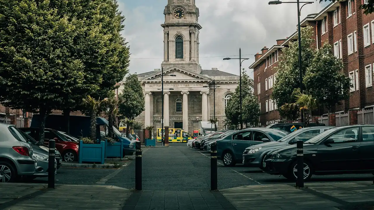 A square in Dublin on a cloudy day: cars parked on both sides, brick buildings to the right and a neoclassical church at the far end