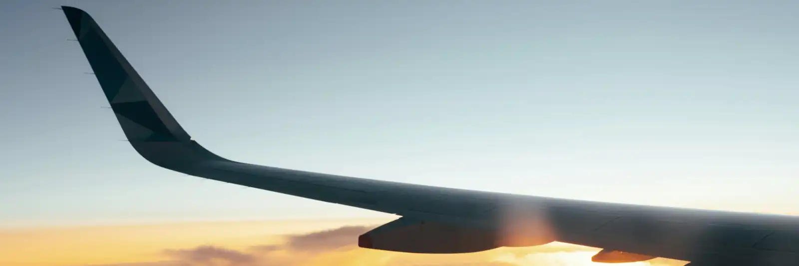 Asa de avião contra o céu no amanhecer, com uma faixa âmbar no horizonte