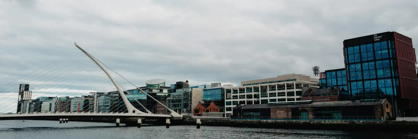 The Docklands district in Dublin seen from the River Liffey, with the Samuel Beckett Bridge on the left and the glass office buildings along the quay.
