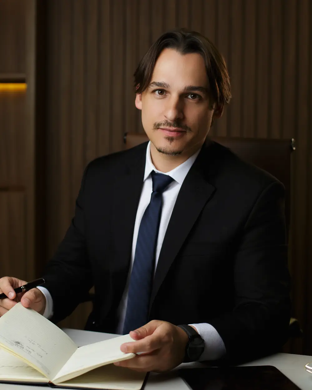 Rafael Dantas in a suit, at his office desk, taking notes in a notebook